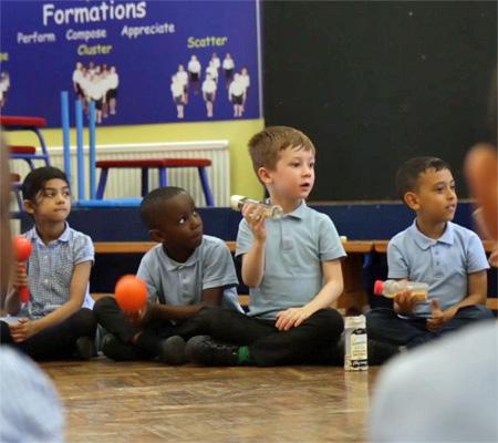 Young children in school uniform seated on the floor with hand percussion