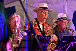 Three saxophone players from Ran Kan Kan, one woman, and two men with straw hats on.
