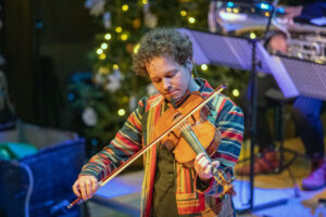 Ultan O'Brien playing fiddle in front of a lit Christmas tree