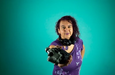 Portrait of Maya Chowdhry holding out a camera towards the viewer