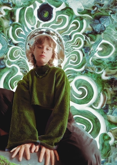 Portrait of Kat Pegler sat on a rock in front of a swirling green background